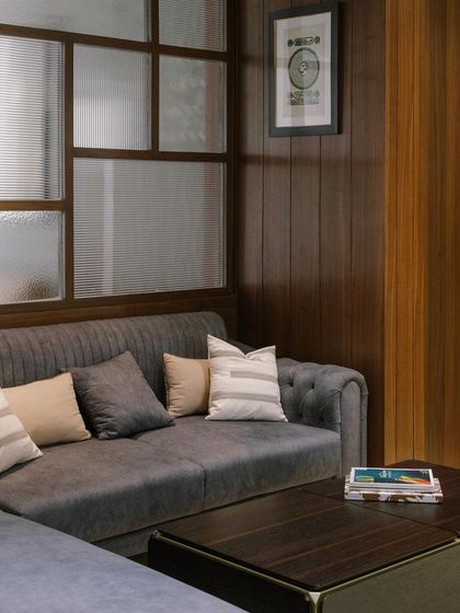 A fluted glass partition provides visual privacy for this lounge area while allowing natural light to filter through. The rich wood frame and tufted sofa create a warm, textural contrast.