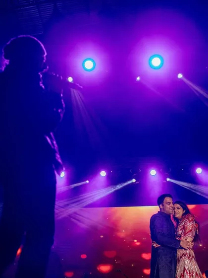 Riya and Neetish embrace as Shekhar Ravijani performs in Barcelona. The silhouette against the purple stage lights creates a dramatic and emotional concert-style wedding photo.