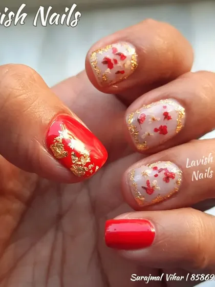 A festive design on short, natural nails, with red polish, gold foil, and hand-painted red floral details.
