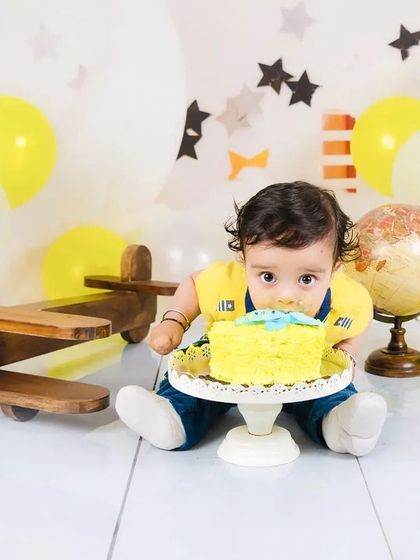 This little aviator is digging right into his cake! A fun and messy moment from a travel-themed first birthday shoot.