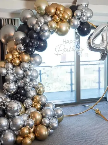 A 40th birthday party with a modern black, gold, and silver balloon arch. The setup is arranged on a circular frame in front of a large window.