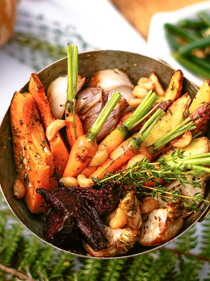 A pan of roasted root vegetables, including carrots and pumpkin, seasoned with fresh thyme. A classic and essential side dish for any Thanksgiving feast.