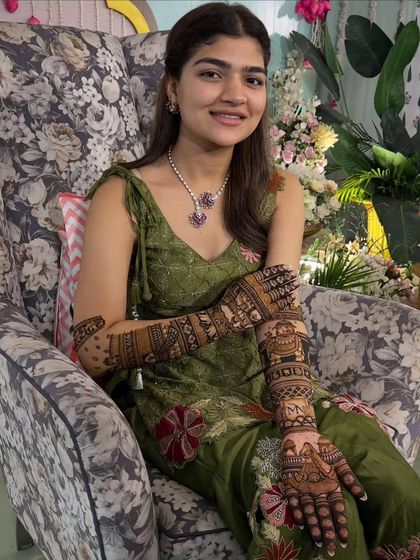 A beautiful bride sitting gracefully with her full-arm mehandi. Her serene smile and the intricate design create a picture of elegance.