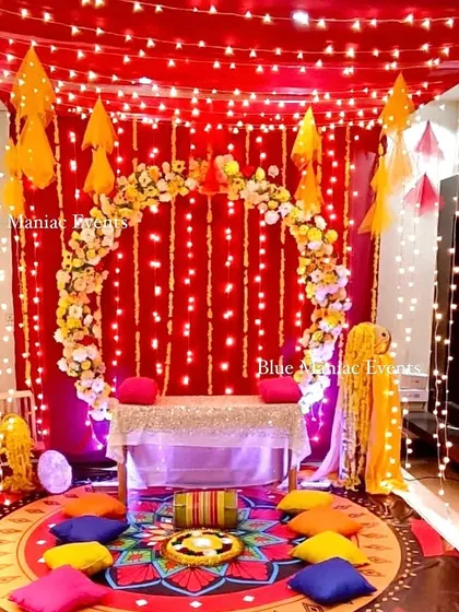A magical Mehendi setup with a red and yellow theme, illuminated by strings of fairy lights covering the ceiling and backdrop. The colorful floor seating completes the cozy and festive look.