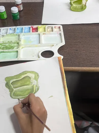 A student works on a detailed painting of a sliced capsicum. Our classes guide students on how to use watercolors to create depth and realism in their still life compositions.