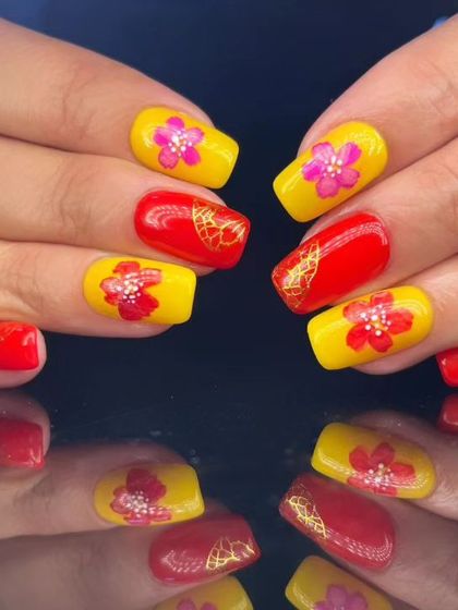 A vibrant Chinese New Year-inspired design with bright red and yellow nails, featuring hand-painted pink flowers and gold accents.
