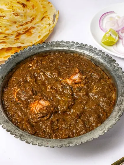 A complete meal of a Mughlai chicken curry, laccha paratha, and a side of onions, arranged as a flatlay. This type of shot is great for showing meal combos and thalis.