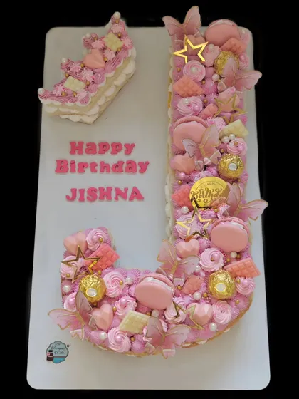 A monogram cake in the shape of the letter 'J'. This tart-style cake is layered with cream and loaded with macarons, chocolates, and other treats.
