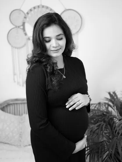 A simple and elegant black and white solo maternity portrait. The focus is on the mother's serene expression and the beautiful shape of her baby bump.