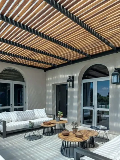A stylish rafter pergola provides filtered sunlight for this chic patio seating area. The design complements the modern architecture of the home, creating an inviting and comfortable space for outdoor relaxation.