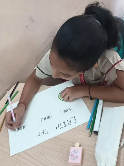 A student works on her Earth Day poster, carefully writing the words "Reduce, Reuse, Recycle," internalizing the core message of sustainability.