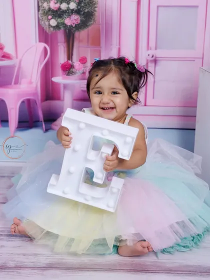 This little girl's smile is infectious as she holds up the letter 'E' in her pastel rainbow tutu during her first birthday session.