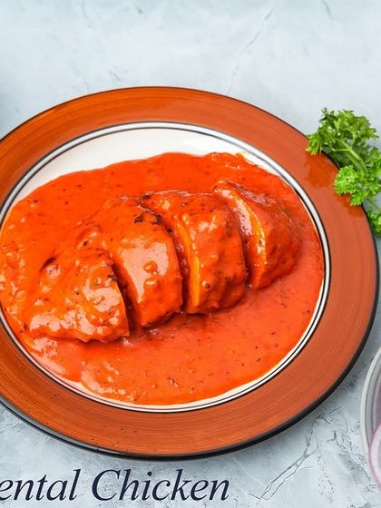 A plated view of our Oriental Chicken. You can see the stuffed chicken breast, sliced to show the filling, and generously coated in a smooth, orange gravy.