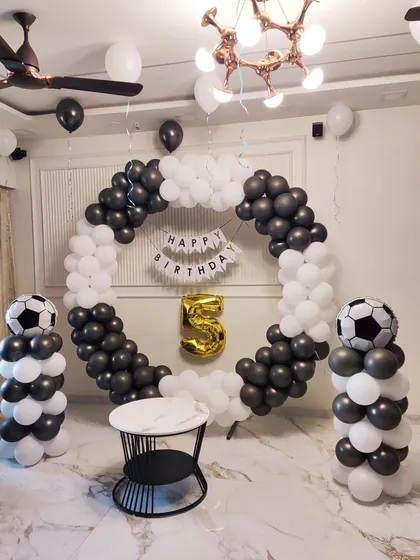 For a 5th birthday, I designed this sharp football-themed decoration. The setup uses a black and white balloon ring, matching balloon pillars topped with football balloons, and a gold '5' foil balloon to bring the sporty theme to life.