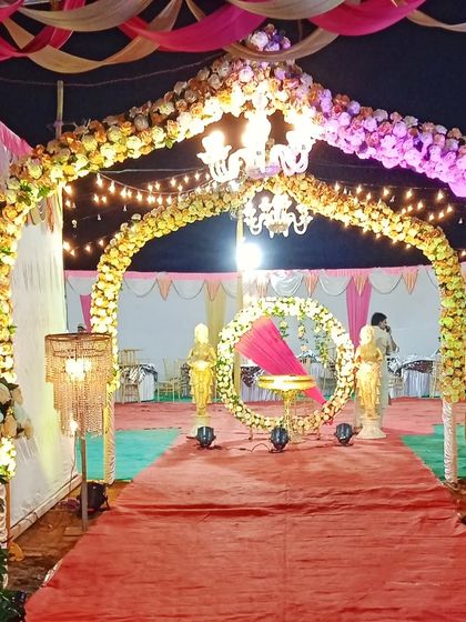 A floral archway entrance for a wedding, illuminated by a chandelier and leading to the main event area with a red carpet.