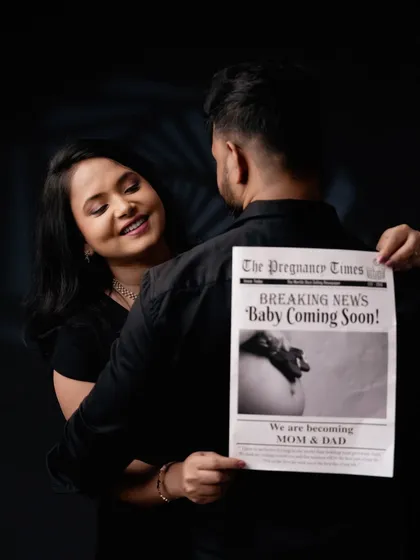 A fun and creative pregnancy announcement. The couple uses a custom "The Pregnancy Times" newspaper prop to share their exciting news in a memorable way.