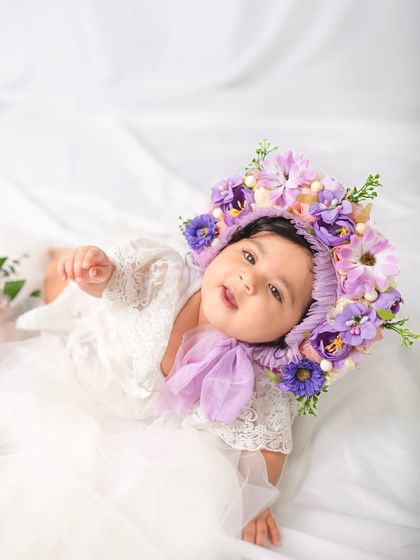 A beautiful overhead shot of an eight-month-old baby lying down, with her stunning floral bonnet as the main focus.