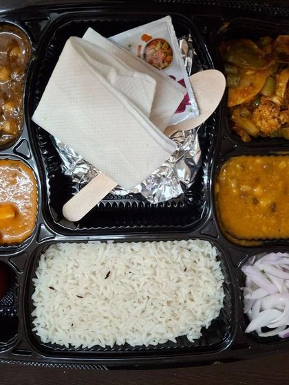 An overhead view of a packed meal thali, showing the different compartments for each dish, keeping the food fresh and separate.