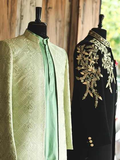 A snapshot from my studio, showing two distinct Indo-Western styles. A mint green jacquard jacket stands next to a black sherwani with bold, gold shoulder embroidery, illustrating the range of my designs.