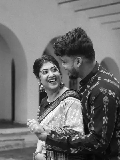 A timeless black and white photo that captures a joyful, candid interaction. Their laughter and shared glance tell a story of easy, comfortable love amidst the arches of Sambalpur.