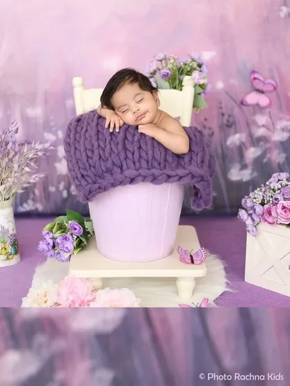 A sweet newborn sleeps in a bucket prop amidst a dreamy lavender field backdrop. This image shows our use of color-coordinated themes and floral elements.