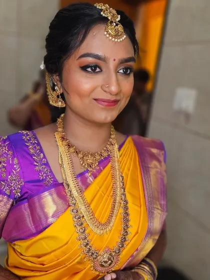 A beautiful muhurtham makeover in a yellow and purple saree. The eye makeup is soft and blended, with a lip color that ties the whole look together.
