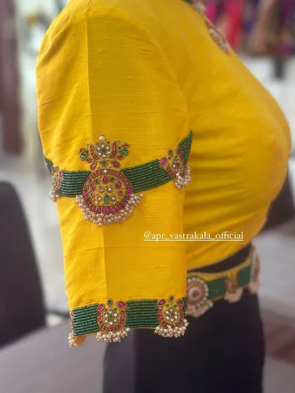 A bright yellow blouse featuring an arm cuff design embroidered with green beads and temple jewellery pendants.