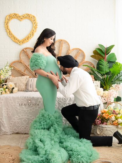 A classic and cherished pose in maternity photography. The father-to-be kneels to kiss the baby bump, showing his connection and love for their unborn child. The mint green gown adds a fresh, soft touch to the scene.