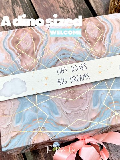 The exterior of the dino-themed hamper, featuring a marbled box and a custom sleeve that reads "Tiny Roars Big Dreams," hinting at the playful adventure inside.