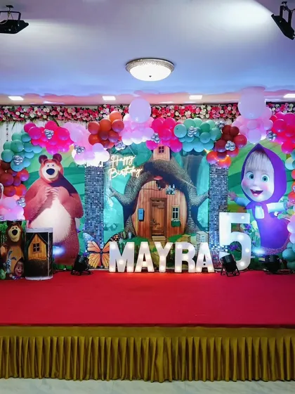 A vibrant Masha and the Bear theme for a 5th birthday. The stage is filled with character cutouts from the show, set against a forest backdrop and framed by a colorful balloon arrangement.