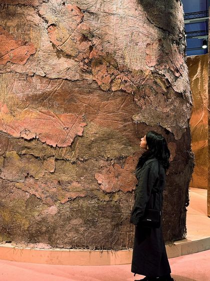 A visitor admires the immense textured wall of the 'Soil' installation. The piece is designed to be a sensorial experience, inviting touch and close inspection.