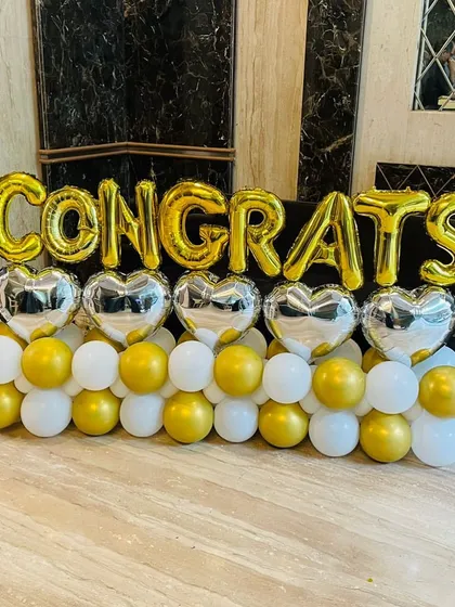 Say 'Congrats' in a big way! This balloon arrangement features gold foil letters, silver hearts, and a base of white and gold balloons for a cheerful and celebratory display.
