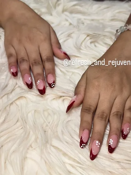 A dramatic French manicure with deep red, almond-shaped tips and delicate white floral accents for a touch of elegance.