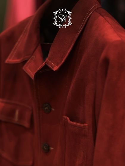 A close-up of a rich, crimson shacket. The lighting and angle emphasize the texture and deep color of the fabric, showcasing a piece of understated luxury.