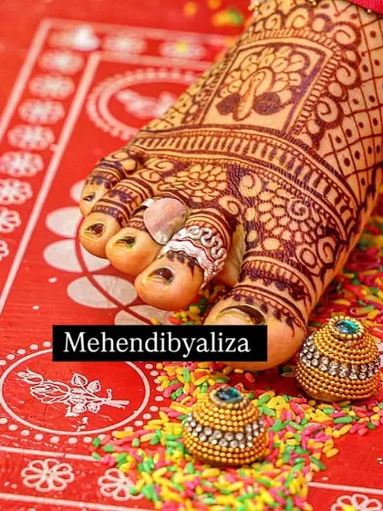 A close-up of a bride's feet with a rich, dark henna stain. The color is absolutely perfect against the red alta.