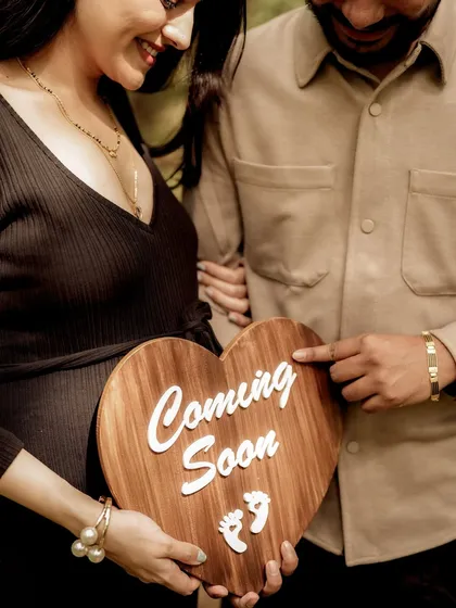 A close-up on the "Coming Soon" sign held against the baby bump. The dad-to-be's finger pointing to the sign adds a playful and direct touch.