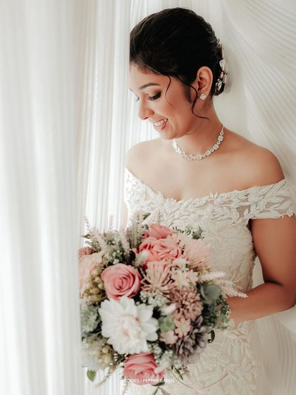 The bride, Shilpa, looking down at her beautiful bouquet. The soft, natural light from the window creates a serene and angelic portrait.
