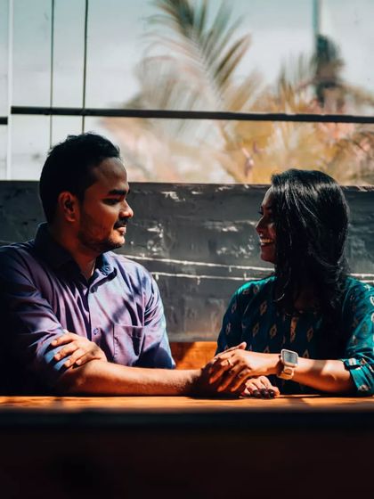 A couple shares an intimate conversation across a table, with beautiful natural light coming through the window. Cafe shoots offer a cozy and timeless setting for portraits.
