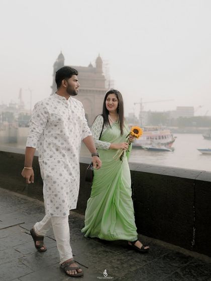 A candid walking shot along the Mumbai waterfront, with the Gateway of India and boats in the background.