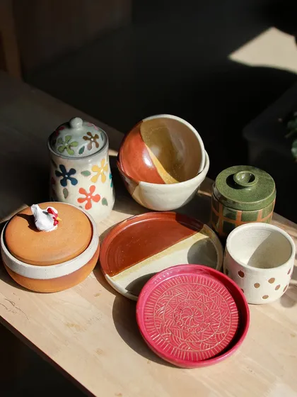 A vibrant collection of lidded jars, plates, and bowls, showcasing a variety of surface decoration techniques like stamping and hand painting.