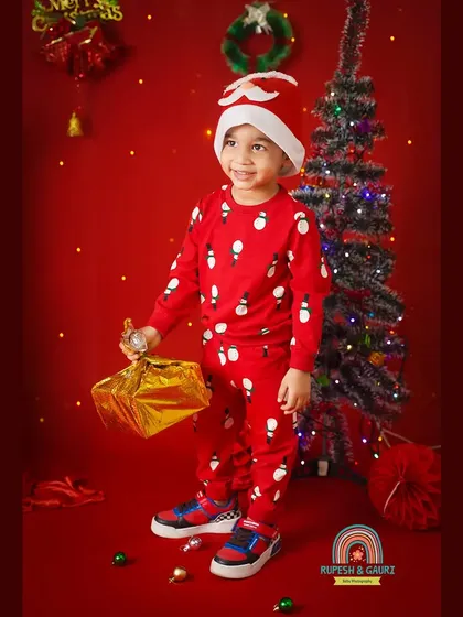 Dressed in a snowman sweater and Santa hat, this little boy is holding a golden present, full of Christmas excitement.