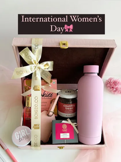 A premium Women's Day hamper in a pink leather-finish trunk. It's filled with a pink water bottle, a "Girl Boss" badge, coffee, cookies, and other curated items.