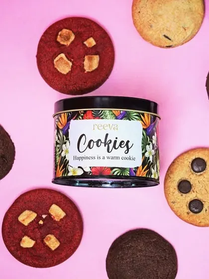 A creative flat lay of various cookies arranged around the product's tin packaging on a bright pink background. This bold, graphic style is designed to grab attention on social media feeds.