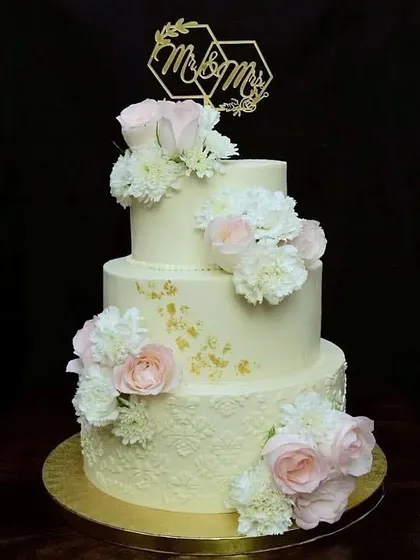 There is something timeless about a three-tier wedding cake. This one features delicate stenciled buttercream, fresh pink and white roses, and a custom "Mr & Mrs" topper, making it a classic and romantic choice for a wedding.