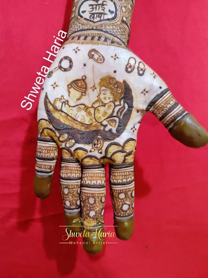 A clear view of the palm from a custom godh bharai mehendi design. It features a depiction of a baby sleeping on the moon, surrounded by baby-themed elements like a rattle, safety pin, and tiny shoes.
