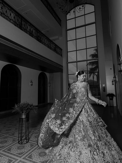 A dramatic black and white portrait of the bride in a grand hall, her lehenga creating a beautiful silhouette.