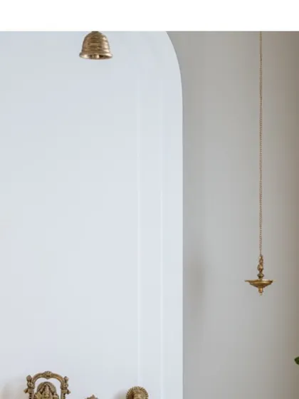 A detail of the mandir, showing the brass bell and hanging lamp against the clean white arched niche. These traditional elements are treated with modern simplicity.