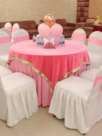 Guest table setup with pink tablecloths, white chair covers with pink sashes, and a simple balloon centerpiece.
