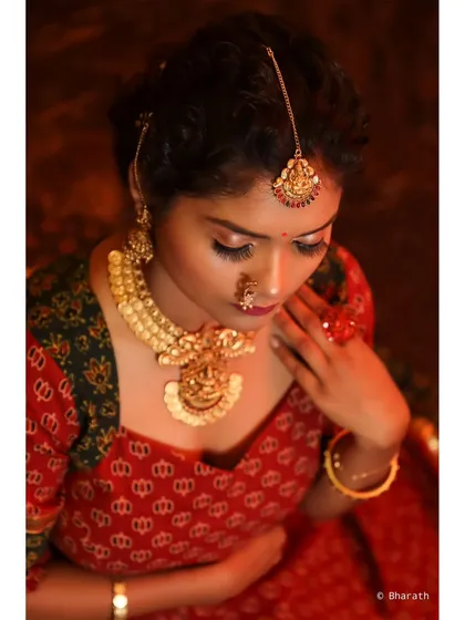 A close-up, high-angle portrait that creates a dramatic and intimate feel. The warm lighting enhances the golden tones of the jewelry and the red fabric.