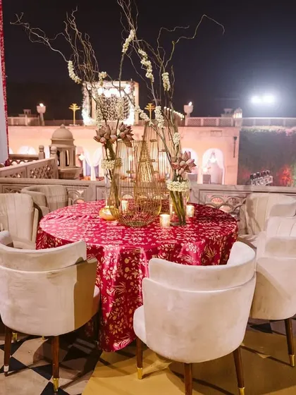 An elegant outdoor seating arrangement for a welcome dinner in Agra. The table is set with a beautiful patterned tablecloth and floral centerpieces, overlooking the venue's stunning architecture.